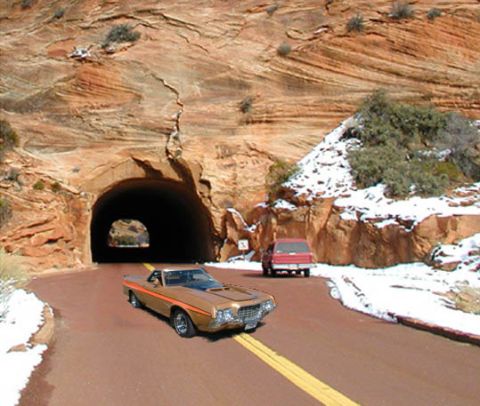 1971 Ford Ranchero - A gold Ford Ranchero with orange stripes drives on a road near a tunnel, with a red pickup truck following.