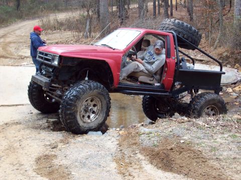 1978 Ford Bronco - A heavily modified red pickup truck attempts to cross a water obstacle on a dirt trail.