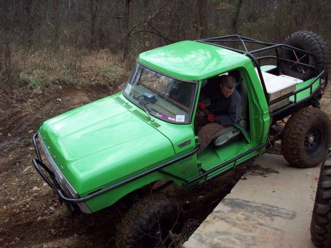 1978 Ford Bronco - This modified truck, likely from the early to mid-1970s, navigates an obstacle with its roll cage and off-road tires visible.
