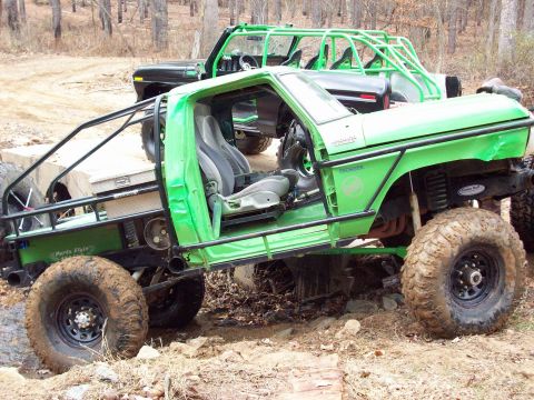 1978 Ford Bronco - Two heavily modified off-road vehicles, including a 1978 Ford Bronco, are parked on uneven terrain.