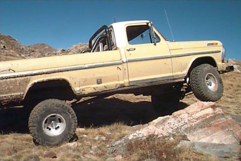 1994 Ford Bronco - This lifted Ford F-Series pickup truck is navigating a rocky terrain under a clear blue sky.
