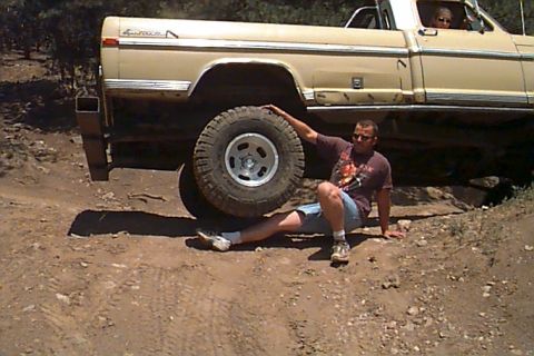 1994 Ford Bronco - Man poses with a lifted pickup truck, showing off its large tire and off-road capability.