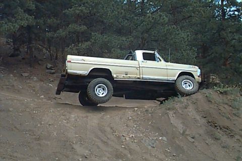 1994 Ford Bronco - This lifted Ford pickup truck navigates an off-road trail with one wheel in the air.