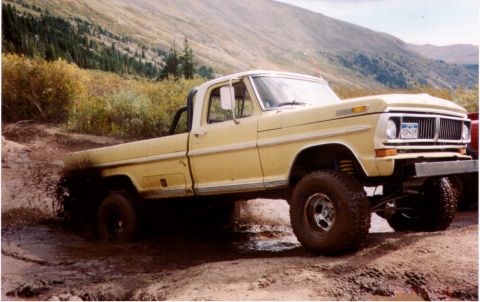 1994 Ford Bronco - This lifted Ford F-Series truck is navigating a muddy trail in a mountainous area.