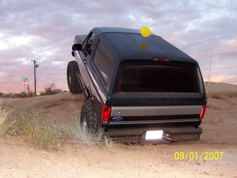 1994 Ford Bronco - A lifted Ford Bronco navigates a sandy incline under a cloudy sky.