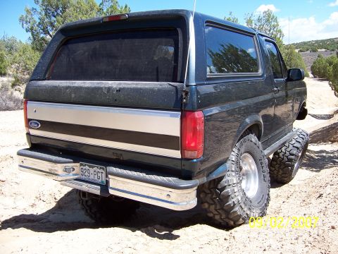 1994 Ford Bronco - This lifted Ford Bronco, likely a 1992-1996 model, is photographed from the rear-right on a dusty trail.