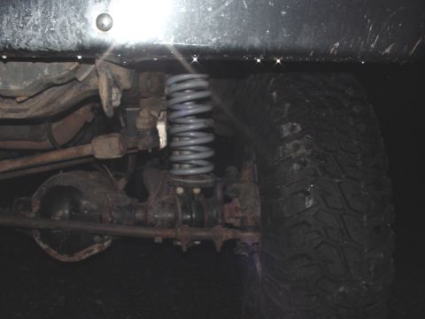 1979 Ford Bronco - The underside of a vehicle shows its suspension components, including a coil spring and a tire.
