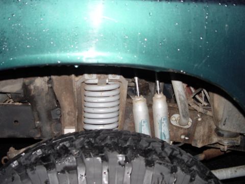 1979 Ford Bronco - Close-up view of the rear suspension system, including a coil spring and shock absorbers, on a green vehicle.