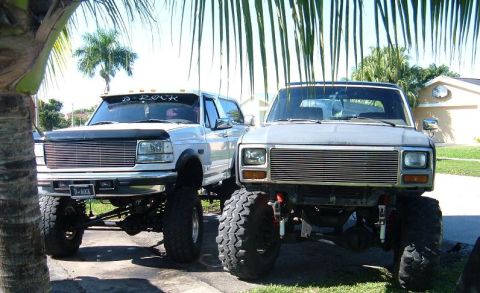 1995 Ford Bronco - Two heavily modified trucks are parked in a driveway, one with custom text on its visor.