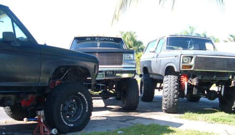 1995 Ford Bronco - A trio of modified trucks, including a 1978 Ford Bronco, are parked on pavement with a tropical background.