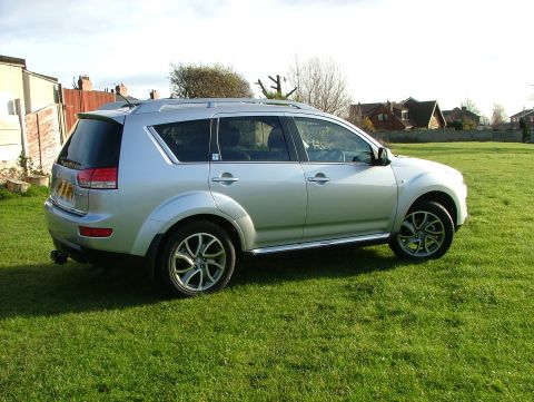 2007 Citroen C-Crosser - A silver SUV is parked on a green lawn with houses visible in the distance under a clear sky.