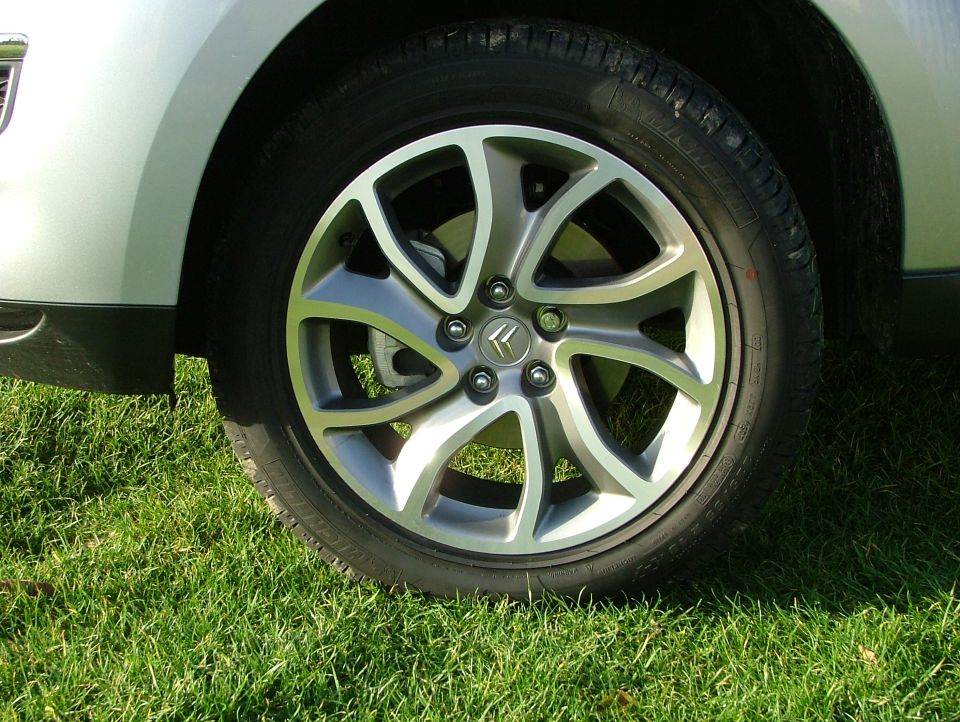 Silver multi-spoke alloy wheel and tire on a car parked on grass