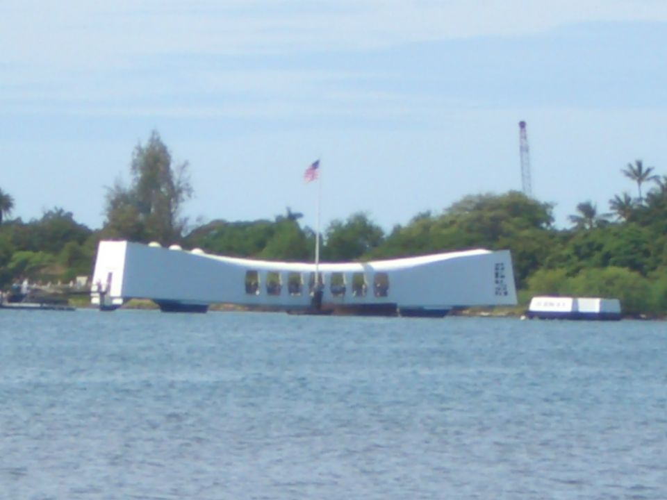 White memorial structure with an American flag on a pole, surrounded by water and trees