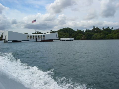 1985 Ford Bronco - The USS Arizona Memorial stands over the water, with a barge nearby and lush green trees on the shore.