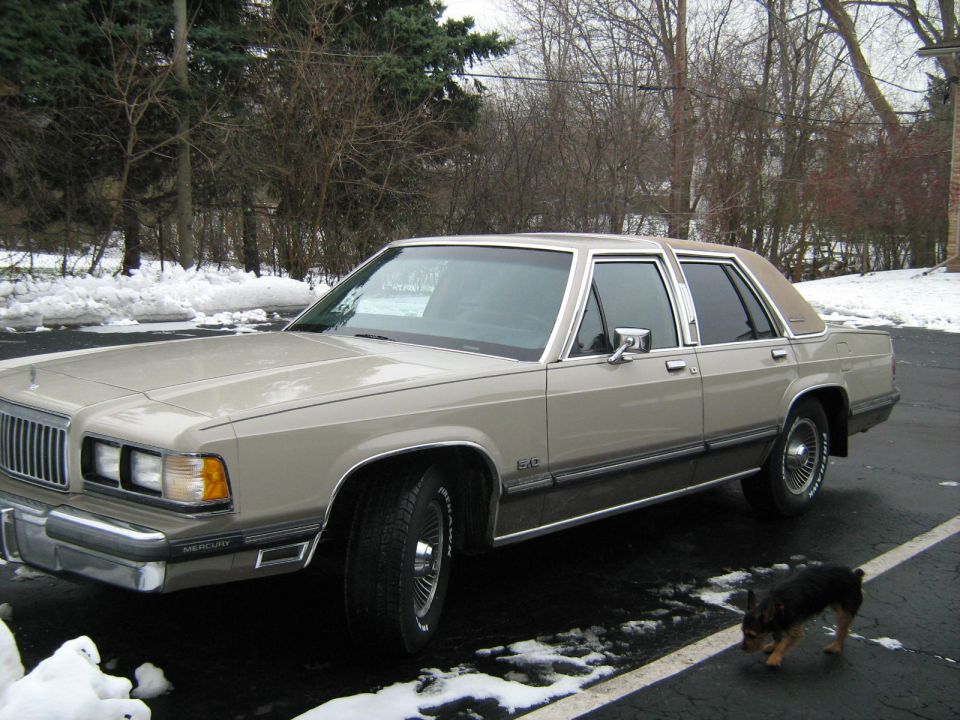Tan 1988 Mercury Grand Marquis sedan parked on asphalt with snow patches, viewed from the front three-quarter angle