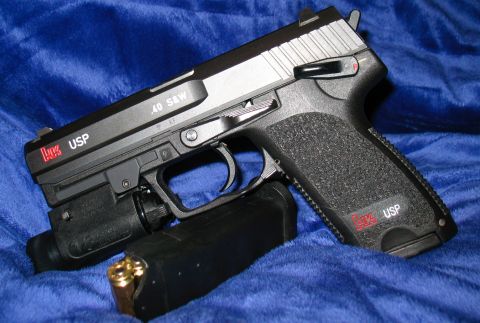 1997 Ford Crown Victoria - A close-up view of an HK USP pistol with a tactical light and a loaded magazine, resting on a blue textured surface.