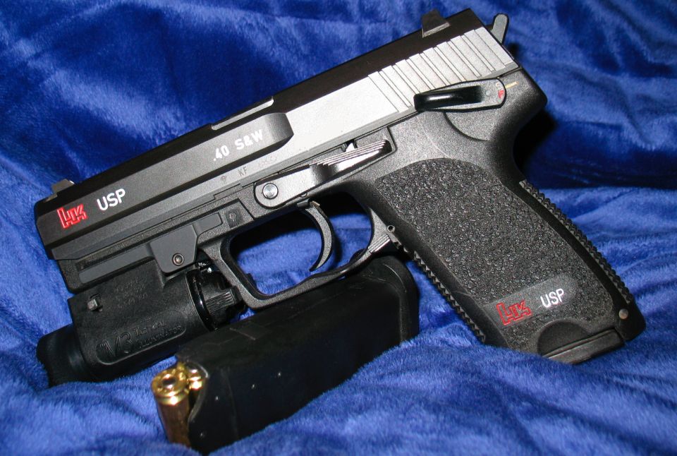 HK USP pistol with .40 S&W slide, attached tactical light, and loaded magazine on blue fabric