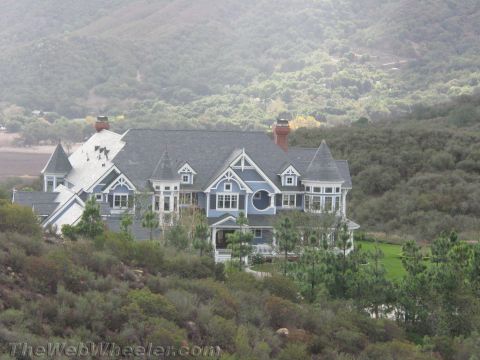 1968 Ford Mustang - A large, ornate house with a blue facade and grey roof sits on a hill surrounded by trees.