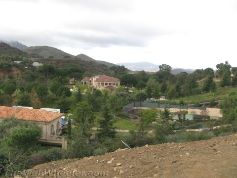 1968 Ford Mustang - A estate is visible amidst lush greenery, a tennis court and distant hills under a cloudy sky.