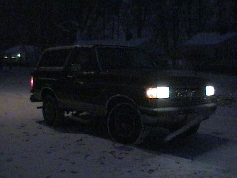 1990 Ford Bronco - Dark 1990 Ford Bronco sits in a snowy area with its headlights illuminated.