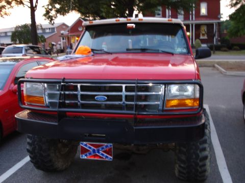 1996 Ford Bronco - A red Ford truck is parked in a lot, showing its front grille, push bar, and large tires.