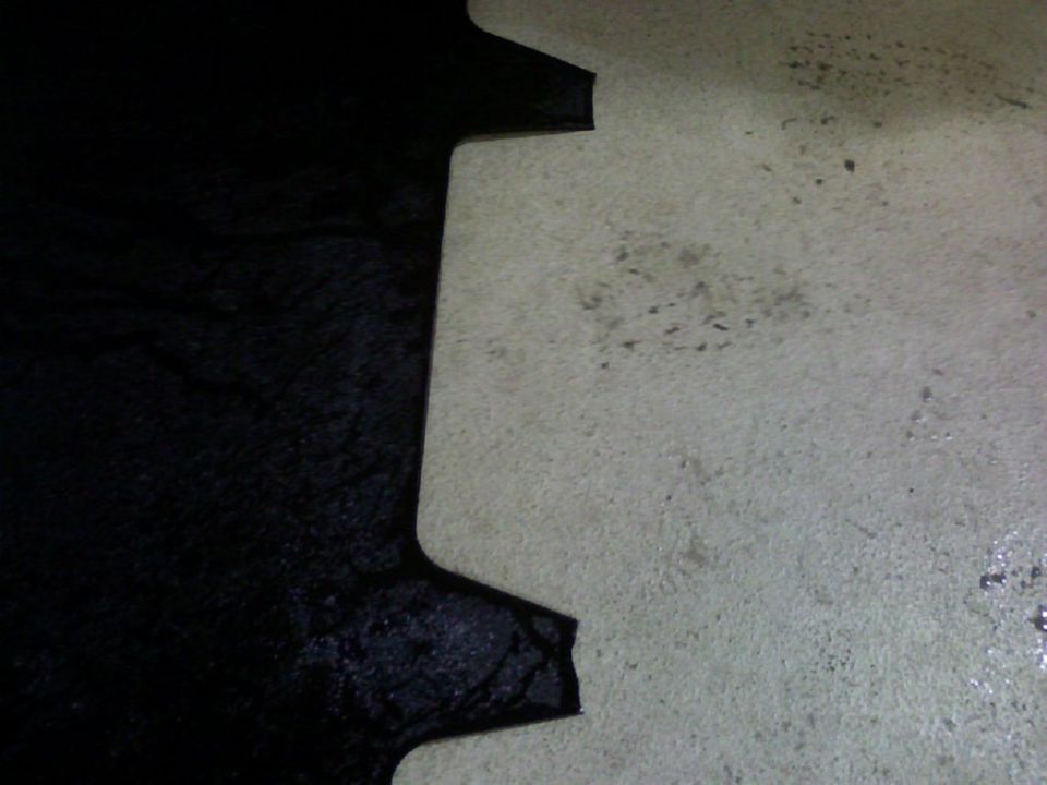 Dark close-up of a notched panel edge against asphalt