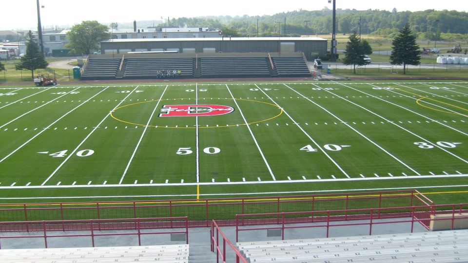 Football field with yard lines and a red logo on the 50-yard line