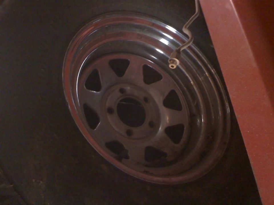 Close-up of a chrome rim with a dark tire and a red body panel. A thin snake is visible near the valve stem