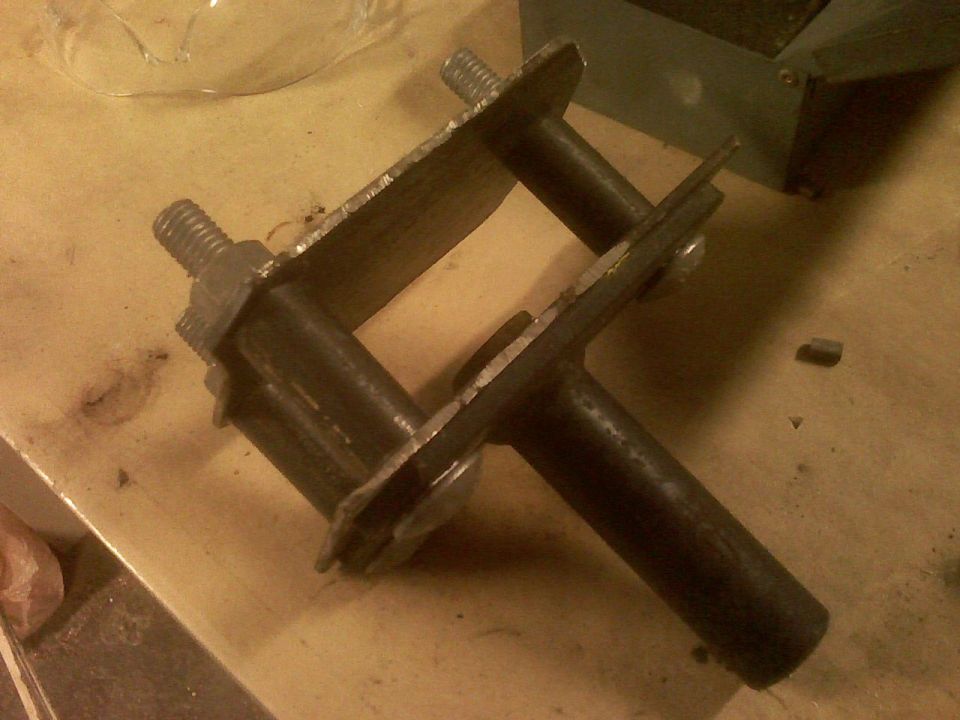 Metal bracket assembly with two bolts and nuts, resting on a wooden surface