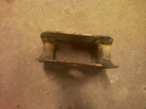 2001 Ford F-150 - A close-up view of a heavily rusted metal bracket, likely a vehicle part, resting on a textured surface.