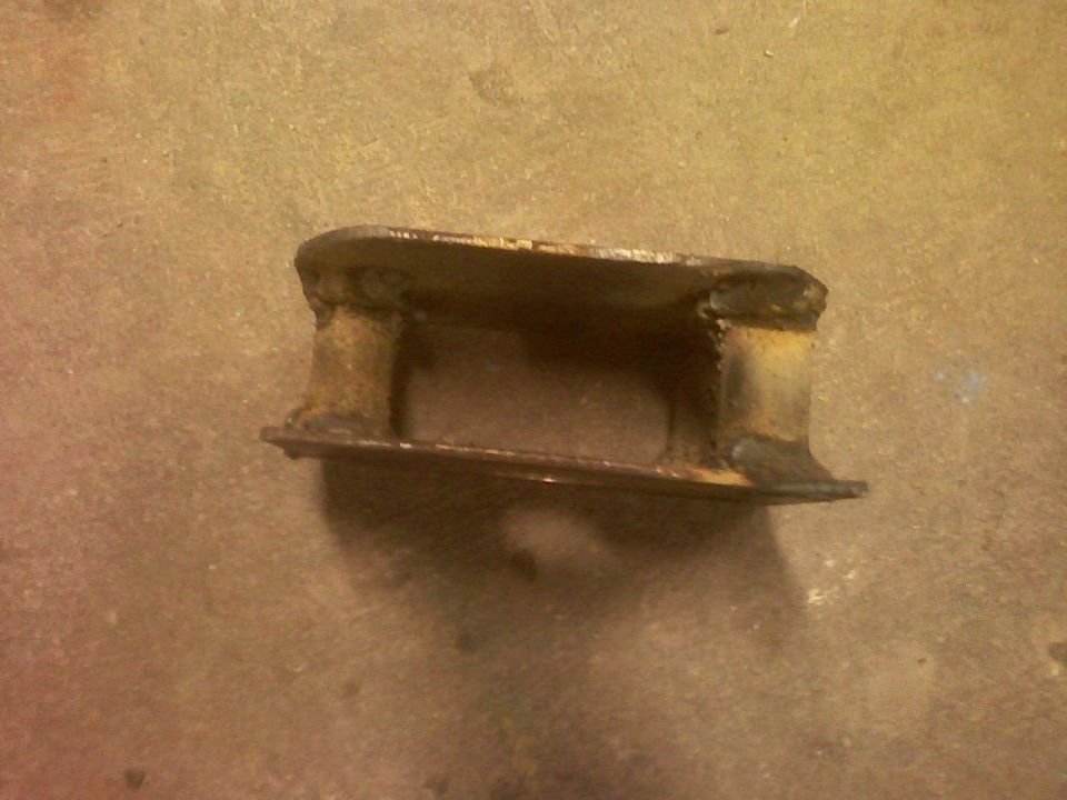 Rusty welded steel bracket with tubular spacers lying on a concrete floor