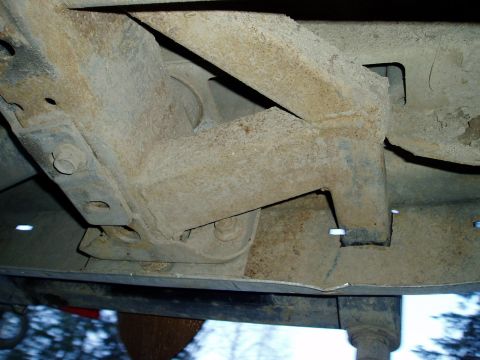 2000 Ford E350 - Close-up view of the rusted underbody chassis components, showing structural elements and fasteners.