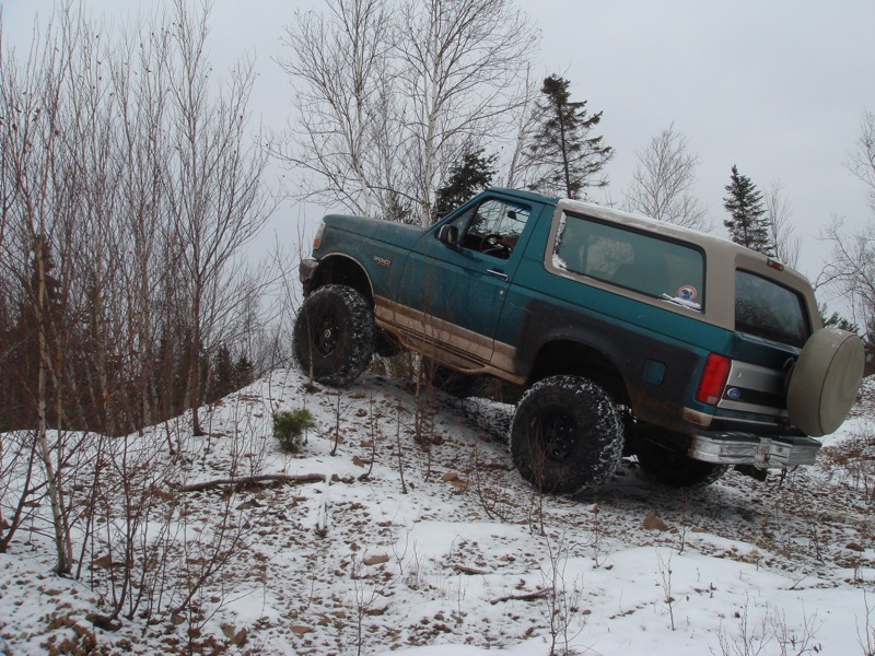Teal Ford Bronco with tan top and large tires climbing a snowy hill