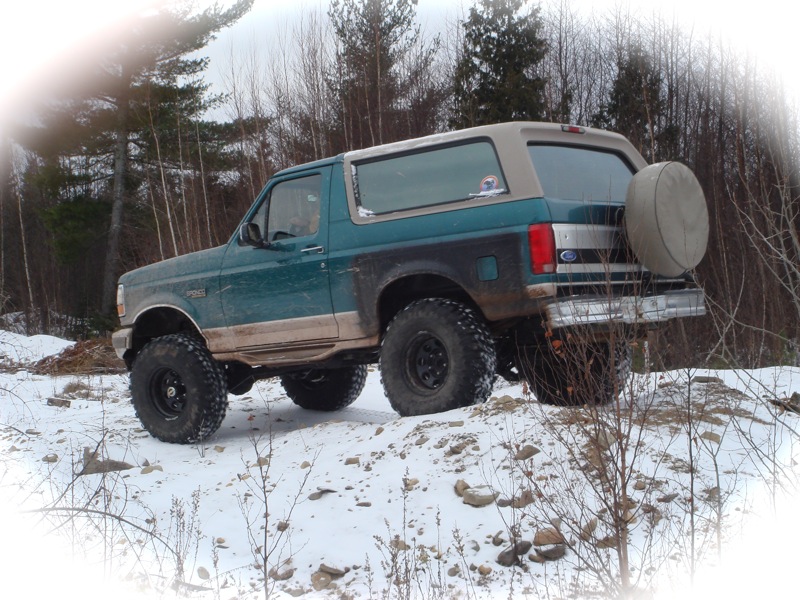 Teal and tan 1996 Ford Bronco with large tires on snowy terrain