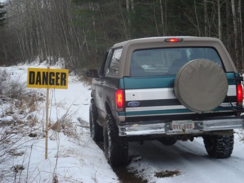 1996 Ford Bronco - A 1996 Ford Bronco drives on a snowy path, passing a yellow danger sign.