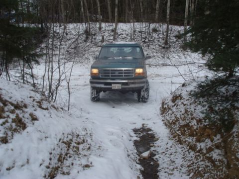 1996 Ford Bronco - A green Ford truck navigates a snowy path with trees in the background.