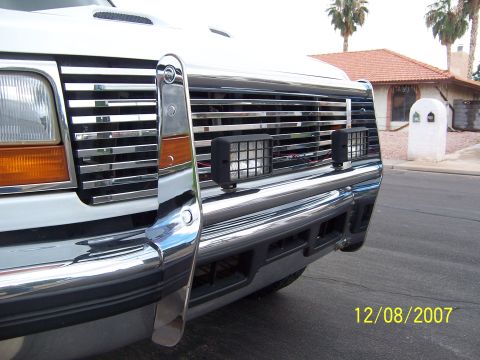 1996 Ford Bronco - Close-up of a truck's front end, a chrome grille guard and auxiliary lights, with a house in the background.