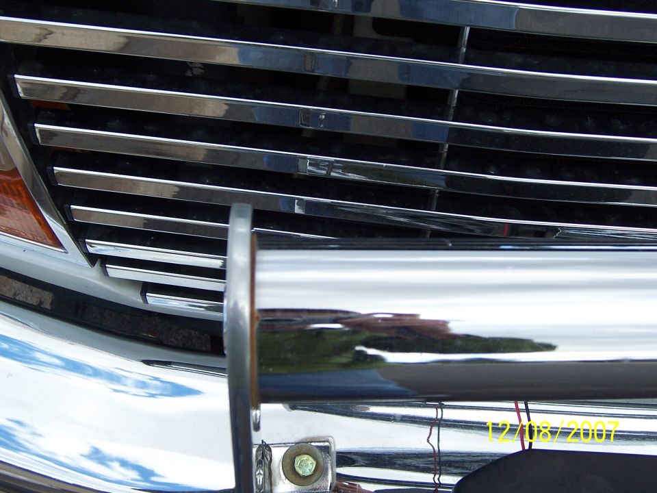 Close-up of chrome grille, bumper and tube brush guard bolted to a truck front end