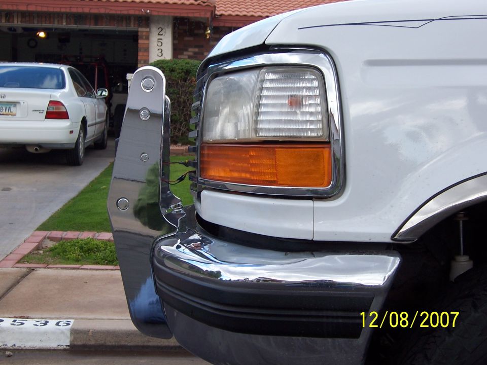 Front corner of white Ford truck showing headlight, amber turn signal and chrome bumper bracket