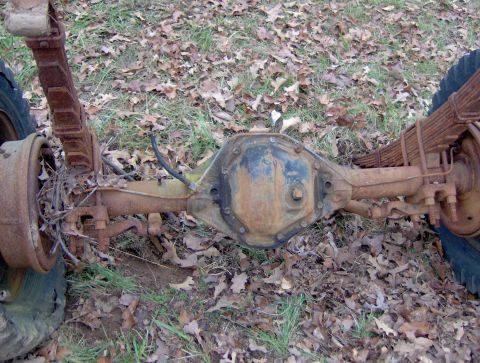 1978 Ford Bronco - A rusty rear axle assembly with leaf springs and drum brakes is shown in a grassy, leaf-covered area.