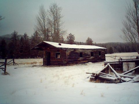 1990 Ford Bronco - A rustic log cabin sits in a snow-covered field under a cloudy sky, with trees and a wooden fence nearby.