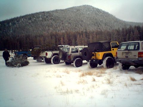 1990 Ford Bronco - A group of off-road vehicles are parked in a snowy landscape, with a person carrying a Christmas tree.