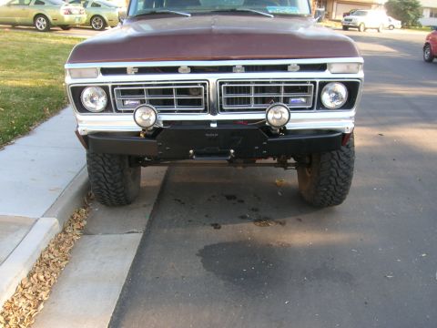 1979 Ford Bronco - Front view of a dark maroon/brown Ford truck with a chrome grille reading 'FORD', round headlights, and a pair of round auxiliary driving l…