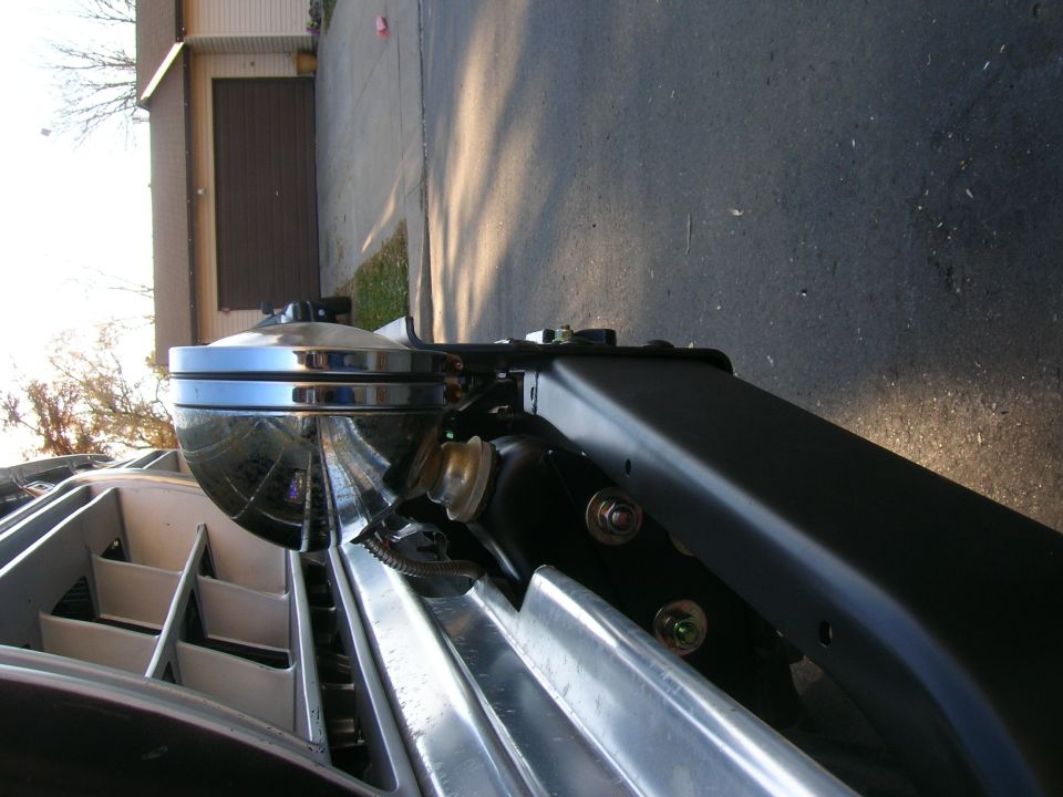 Chrome headlight housing and part of a silver grille with horizontal slats