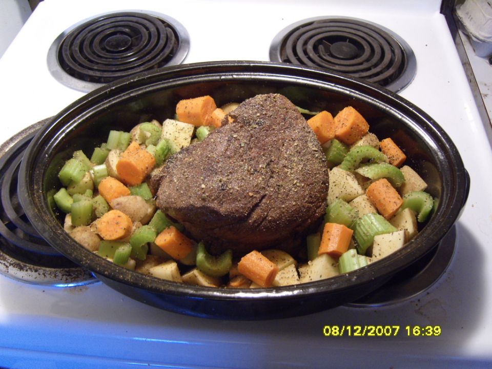Pot roast with carrots and celery in a roasting pan on a stovetop
