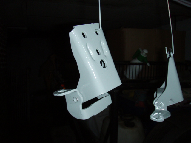 Two white painted door hinges hanging, one in foreground, another in background