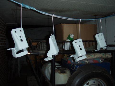 1995 Ford F-150 - Four freshly painted white door hinge and latch brackets hanging from wire hooks on a rope strung across a dim garage to dry. Stored parts,…