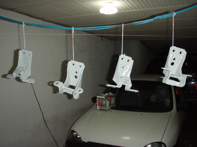 Four white door hinges hanging, with a white car hood visible below