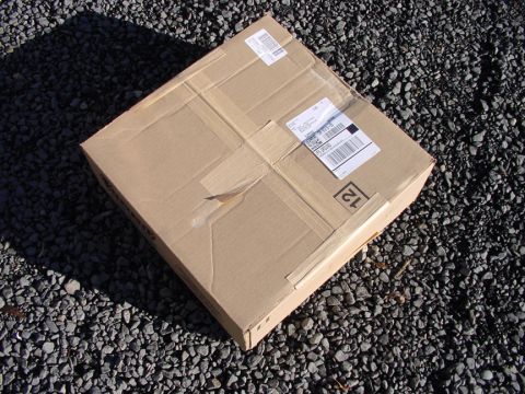 1979 Ford Bronco - A sealed cardboard box sits on a bed of dark gravel, showing shipping labels and a numerical marking.