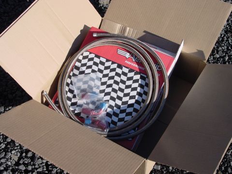 1979 Ford Bronco - A braided hose and fittings are packaged inside a cardboard box, with a checkered flag design on the packaging.
